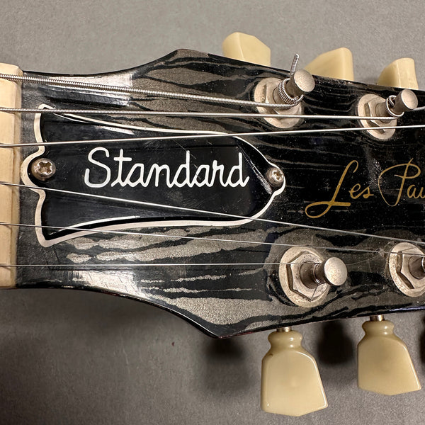 Close-up of Gibson Les Paul Standard guitar headstock with vintage tuning pegs and strings on gray background