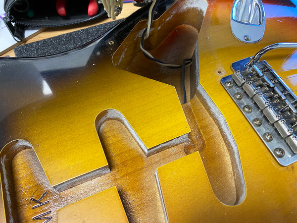 Close-up of sunburst electric guitar body showing routed cavity for pickups and bridge with metal saddles.