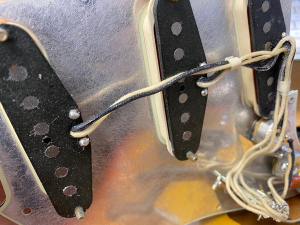 Close-up of vintage electric guitar pickups and wiring inside guitar cavity showing black and white braided cloth wires and pickup magnets