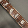 Close-up of guitar fretboard with rosewood wood grain and trapezoid mother-of-pearl inlays, metal frets, and six steel strings on gray background