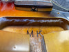 Close-up of the inside cavity of a sunburst electric guitar body showing the wood grain, metal screw, and hand-stamped letters "MK" for guitar identification or branding.