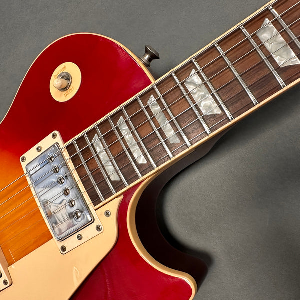 Close-up of red sunburst electric guitar body and fretboard, showcasing white trapezoid inlays and chrome pickup covers on rosewood fingerboard