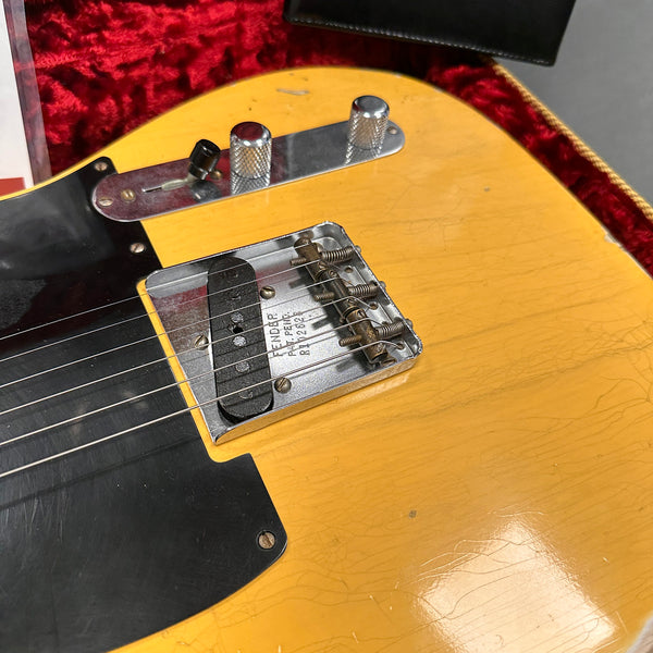 Close-up of vintage Fender Telecaster electric guitar body showing yellow finish, black pickguard, chrome bridge with Fender patent engraving, and control knobs.