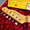 Close-up of Fender Broadcaster guitar headstock with tuning pegs on red plush guitar case lining and yellow electronics specification sheet in background