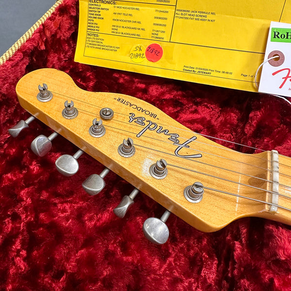 Close-up of Fender Broadcaster guitar headstock with tuning pegs on red plush guitar case lining and yellow electronics specification sheet in background