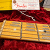 Close-up of vintage Fender guitar maple fretboard with worn dot inlays and strings on red plush case lining, accompanied by Fender hang tag and paperwork