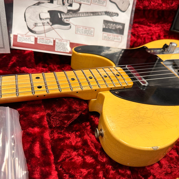Close-up of vintage yellow electric guitar body and maple neck with black pickguard resting on red velvet guitar case interior with guitar schematic in background