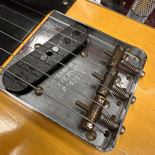 Close-up of vintage Fender Telecaster bridge plate with single-coil pickup, strings, and saddle screws on yellow guitar body