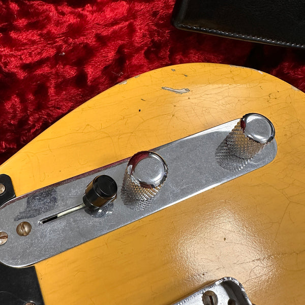 Close-up of vintage yellow electric guitar control plate with chrome volume and tone knobs and black switch on red plush background