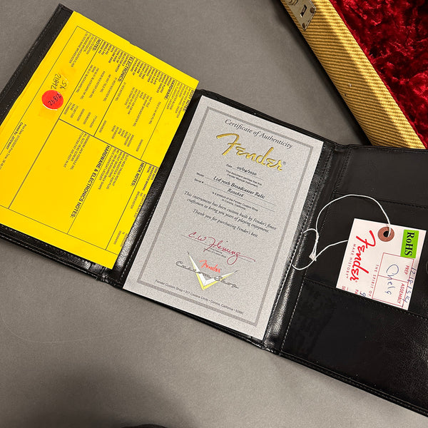 Fender Certificate of Authenticity for Ltd 70th Broadcaster Relic guitar with Fender Custom Shop tag and yellow guitar spec sheet in black leather folder near guitar case interior