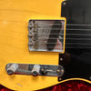 Close-up of vintage Fender Telecaster electric guitar bridge, single-coil pickup, control knobs, and yellow aged finish with black pickguard.