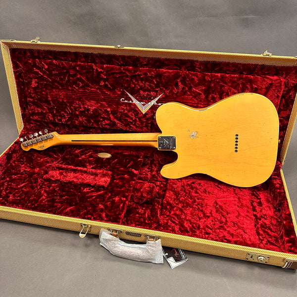 Vintage blonde electric guitar shown from the back resting inside an open tweed hard case with red plush interior lining and Custom Shop logo