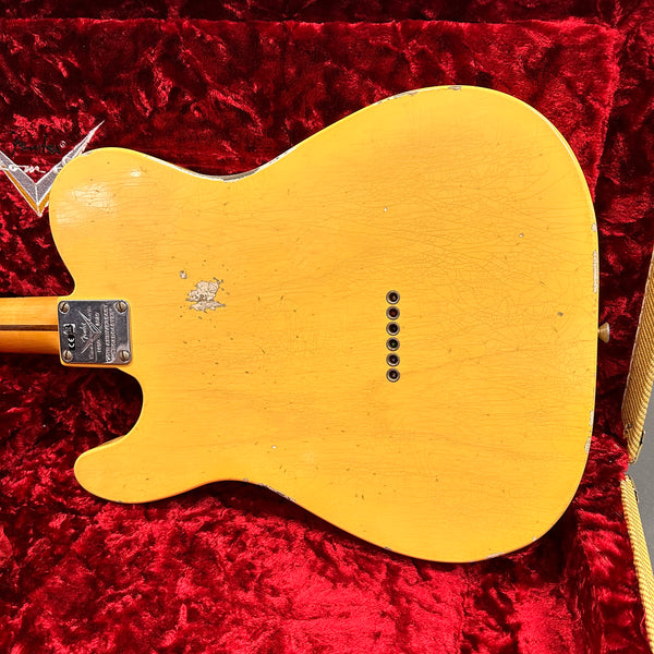 Vintage worn yellow Fender Telecaster guitar body back showing string ferrules and neck plate, placed on red plush guitar case interior