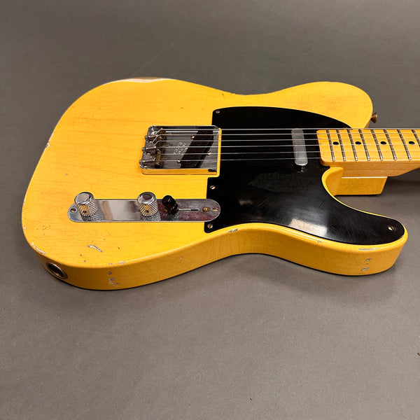 Close-up of vintage worn yellow electric guitar body with black pickguard and chrome knobs on gray background