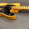 Close-up of vintage yellow electric guitar body and neck with black pickguard and worn finish on gray background