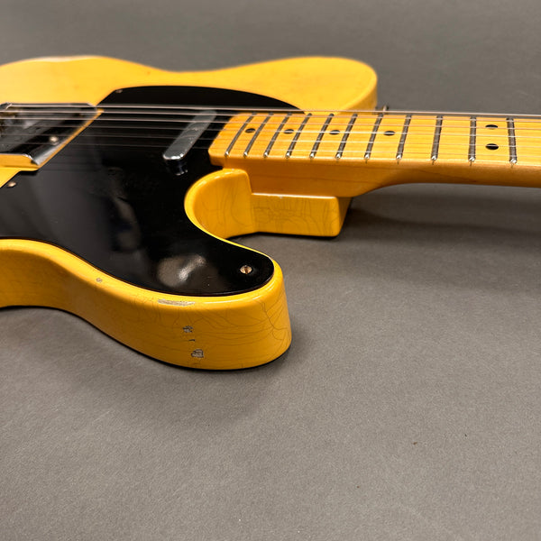 Close-up of vintage yellow electric guitar body and neck with black pickguard and worn finish on gray background