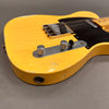 Close-up of vintage yellow electric guitar body with metal control knobs, black pickguard, worn finish, and chrome bridge on gray background