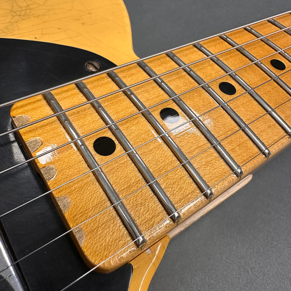 Close-up of vintage electric guitar maple neck with worn fretboard and black dot inlays, showing steel strings and black pickguard.