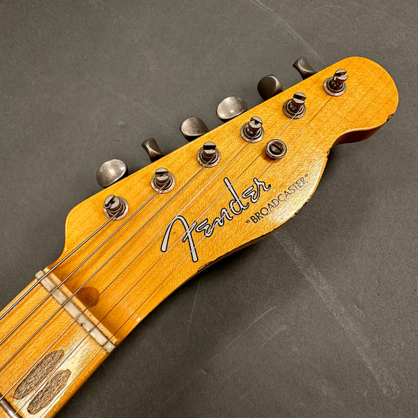 Close-up of vintage Fender Broadcaster guitar headstock with six tuning pegs and worn wooden finish against gray background