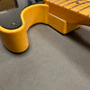 Close-up of vintage yellow electric guitar neck joint showing cracked finish and fretboard details on gray surface