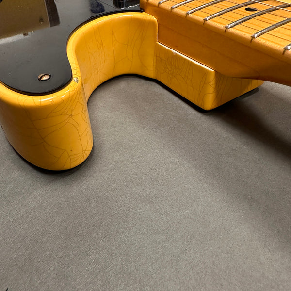 Close-up of vintage yellow electric guitar neck joint showing cracked finish and fretboard details on gray surface