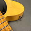 Close-up of vintage yellow electric guitar body with visible finish cracking and strap button, part of maple neck and metal frets on gray background