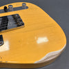 Close-up of a vintage yellow electric guitar body showing wear, cracks in the finish, and chrome control knobs with a black switch on a gray background.