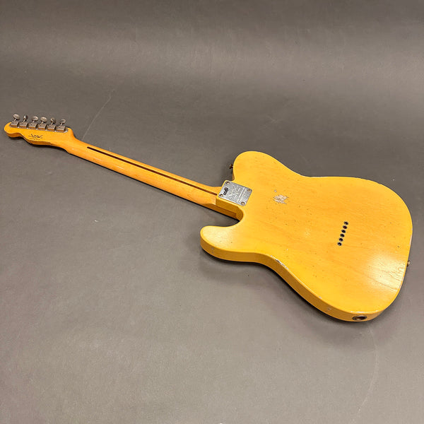 Vintage worn yellow electric guitar with maple neck and six tuning pegs lying face down on gray surface
