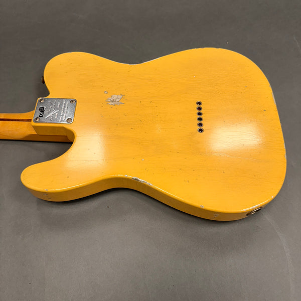 Vintage yellow electric guitar body with visible wear and paint chips, rear view showing string ferrules and neck plate on gray background