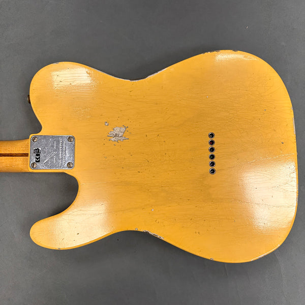 Back view of vintage yellow electric guitar body with string ferrules and neck plate on gray background