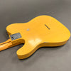 Back view of vintage yellow electric guitar body with worn finish and metal neck plate on gray surface