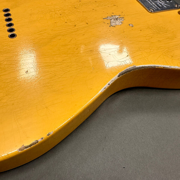 Close-up of vintage yellow electric guitar body showing worn finish and paint chips on the edge, highlighting relic details and aging effect