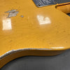 Close-up of worn vintage yellow electric guitar body with paint chips and fine finish cracks near metal neck plate on gray surface