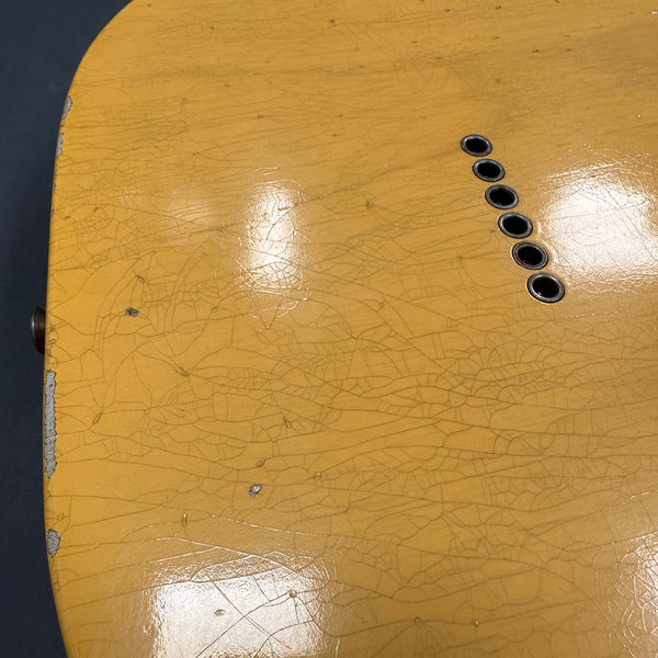 Close-up of vintage worn yellow guitar body showing finish cracks and string ferrules on Coffee House Guitars product listing