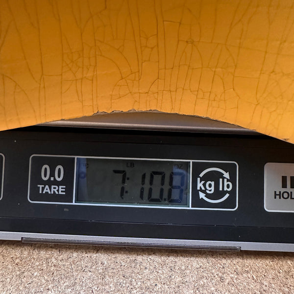 Close-up of digital scale displaying 7 pounds 10.8 ounces weight with guitar body edge showing above the scale