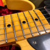 Close-up of vintage electric guitar maple neck and fretboard with metal frets and strings on a cream-colored body