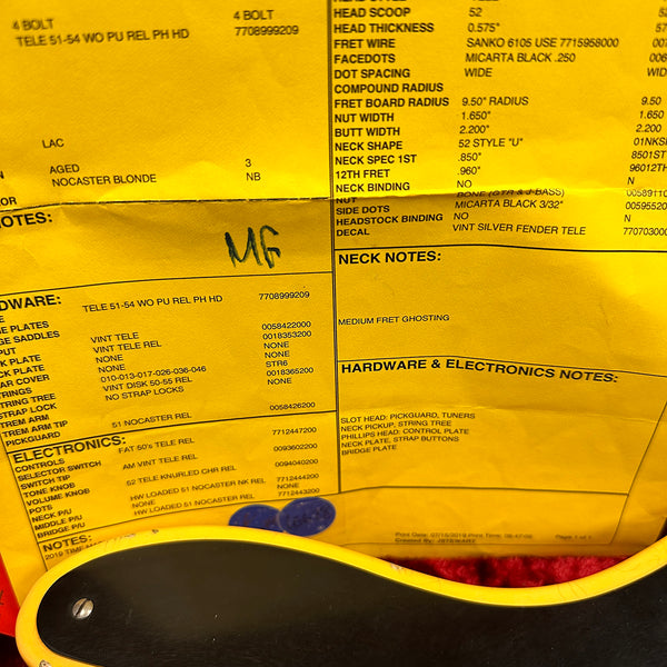 Close-up of a yellow specification sheet for a Fender Telecaster guitar showing detailed hardware, electronics, neck, and pickup notes, partially covered by part of a yellow and black guitar body and a blue guitar pick.