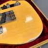 Close-up of vintage yellow electric guitar body with worn edges and visible finish cracks, resting on red velvet-lined guitar case