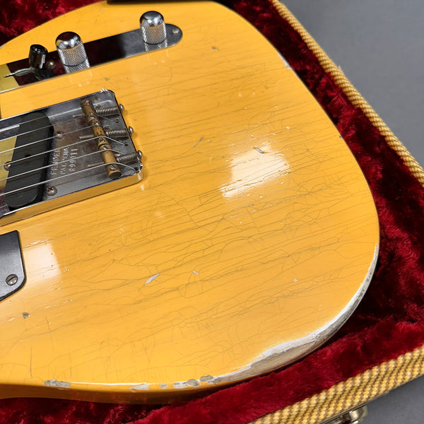 Close-up of vintage yellow electric guitar body with worn edges and visible finish cracks, resting on red velvet-lined guitar case