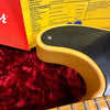 Close-up of a vintage-style Fender guitar body corner with black pickguard, yellow finish, visible wear, set against red plush fabric background, accompanied by Fender electronics specification sheet and manual for Fender guitars.