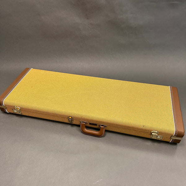 Rectangular vintage yellow tweed guitar case with brown leather handle and corner accents on gray background
