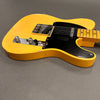 Vintage yellow Fender Telecaster electric guitar with black pickguard and chrome hardware on gray surface