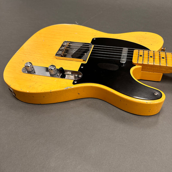 Vintage yellow Fender Telecaster electric guitar with black pickguard and chrome hardware on gray surface