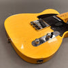 Close-up of vintage yellow electric guitar body with black pickguard, chrome bridge, and control knobs on gray background.