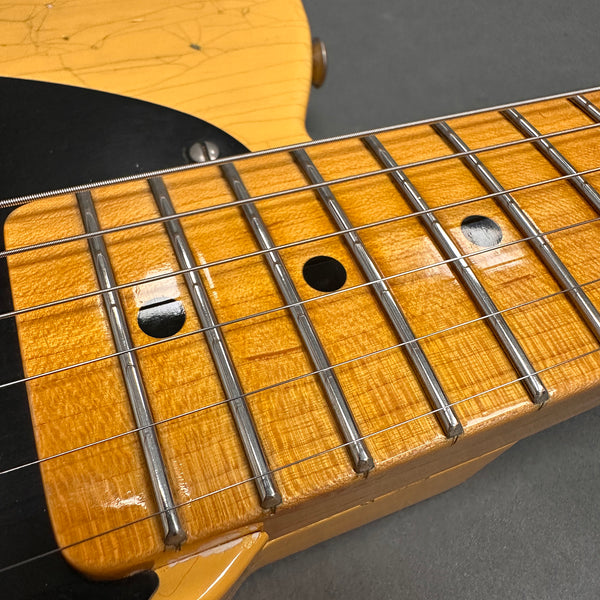 Close-up image of a vintage electric guitar maple neck with worn finish, chrome frets, and black dot inlays on a light amber fretboard.