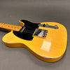 Vintage yellow electric guitar with black pickguard and chrome knobs on grey background, showing worn and chipped body edges.
