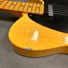 Close-up of worn vintage yellow electric guitar body with black pickguard and chipped paint on gray background