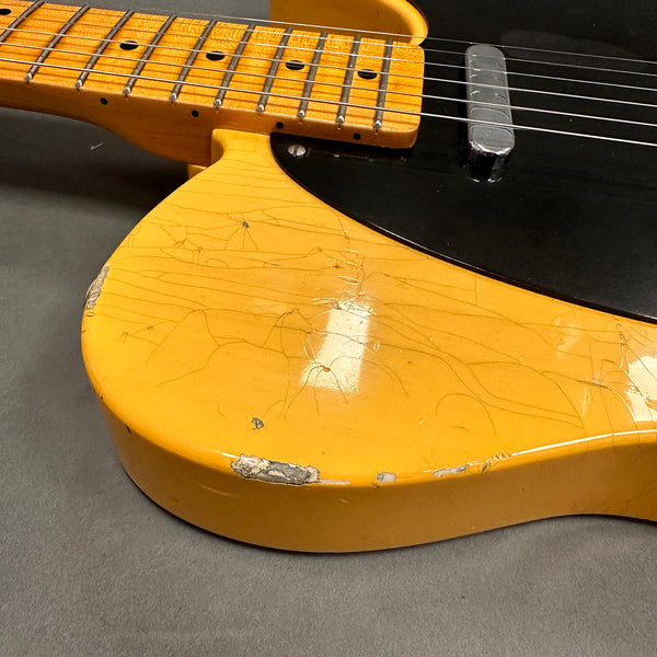 Close-up of worn vintage yellow electric guitar body with black pickguard and chipped paint on gray background