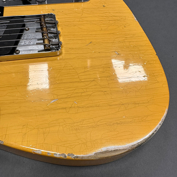 Close-up of vintage yellow electric guitar body with worn edges, checking finish, and metal bridge components, highlighting aged relic condition.