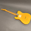Back view of vintage yellow electric guitar with worn finish and bolt-on neck on gray background